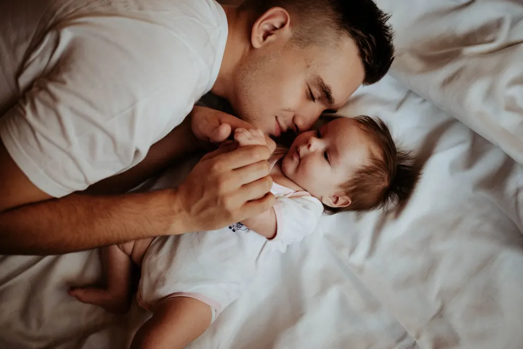 Pappa ligger nära sin bebis i sängen en lugn morgon, när familjen ser över barnförsäkring