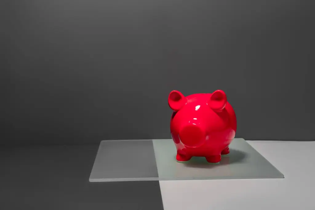 En röd spargris på en glasskiva mot grå bakgrund, symbol för valet mellan att spara och att amortera
