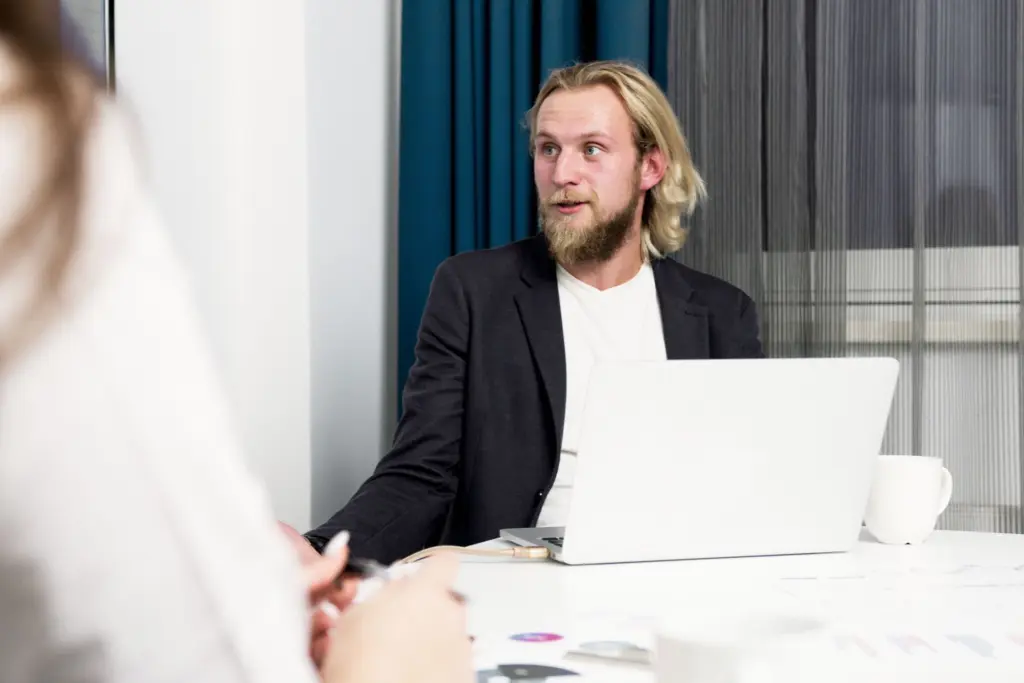 Man i kavaj vid ett mötesbord med laptop, i samtal med en rådgivare