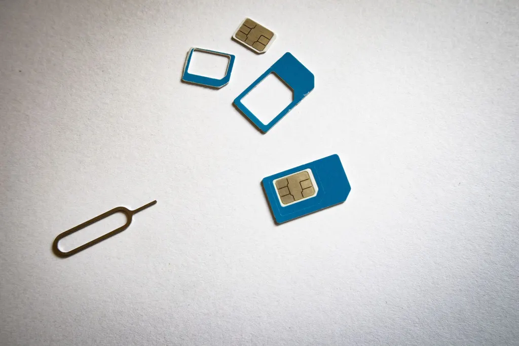 SIM-kort i olika storlekar och en utmatningsnål på en ljus yta, inför byte av mobiloperatör med nummerflytt