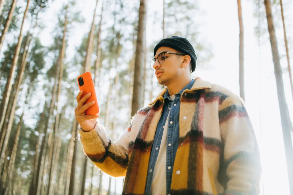 Man i mössa och rutig jacka tittar på sin mobil i en tallskog