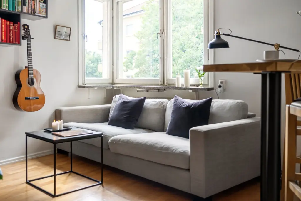 Ljust vardagsrum i en lägenhet med grå soffa, soffbord med levande ljus, gitarr på väggen och bokhylla, en bild för bostad och bohag som delas i en bodelning