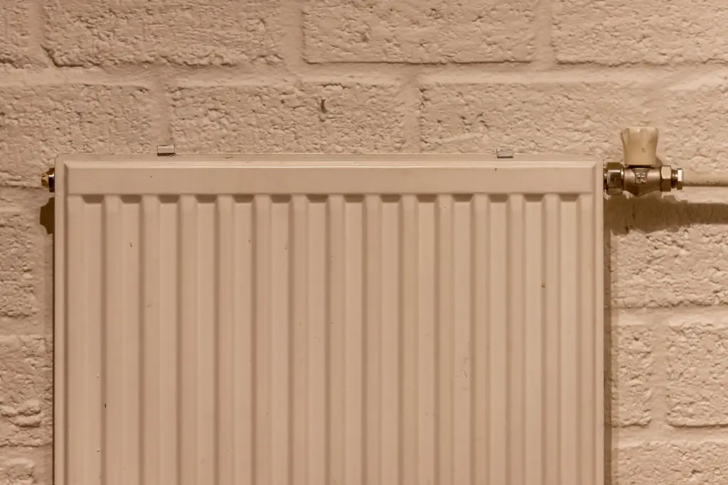 Vitt element med termostatventil mot en målad tegelvägg; ju mer el som går åt, desto mer väger priset per kWh
