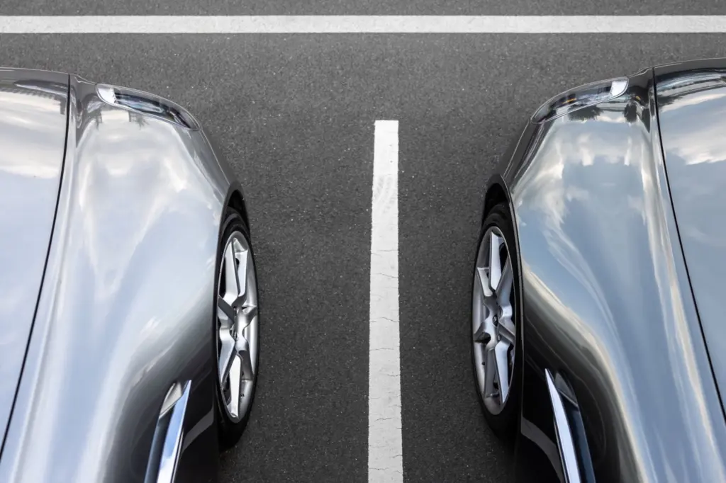 Två silverfärgade bilar parkerade sida vid sida med en vit linje emellan, sedda uppifrån, en bild för jämförelsen av två bilförsäkringar
