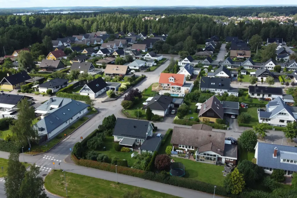 Flygbild över ett svenskt villaområde med trädgårdar och gator, skog och sjöar i bakgrunden, en bild för att välja bolånebank
