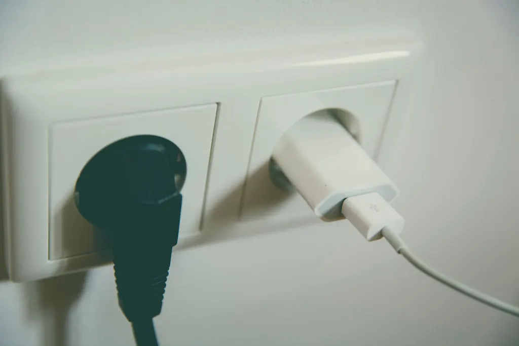 Två stickkontakter i ett vitt eluttag på väggen, jämförelse av elavtalen från Tibber och Greenely