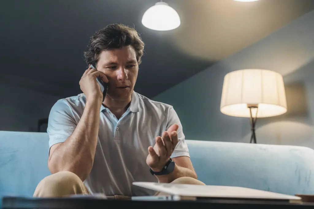 Man i soffan i ett lampupplyst vardagsrum pratar i telefon och gestikulerar tveksamt, som när en elsäljare ringer med ett erbjudande