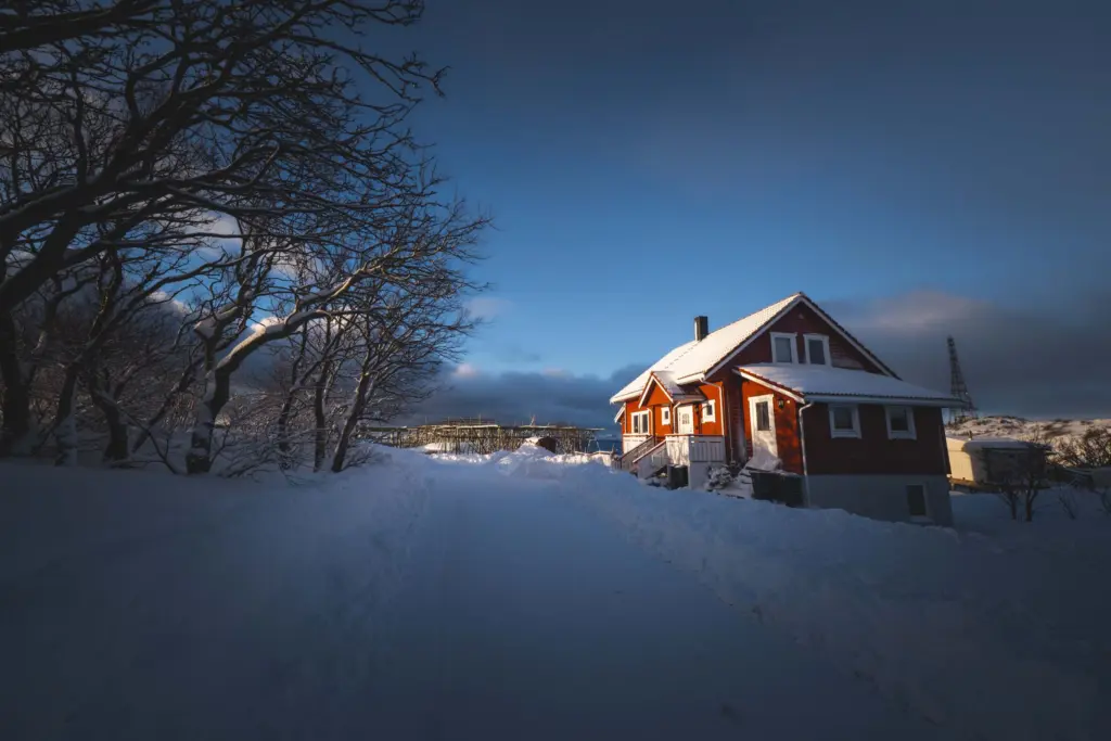 Rött trähus vid en snötäckt väg i kvällsljus en kall vinterdag