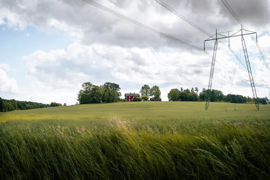 Kraftledning över ett sädesfält med ett rött hus i bakgrunden; energiskatten tas ut på elen som kommer via elnätet