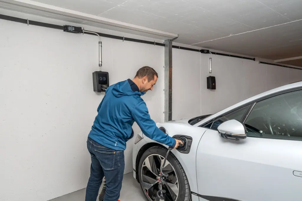Man kopplar in laddkabeln i en elbil vid en laddbox på väggen i ett garage
