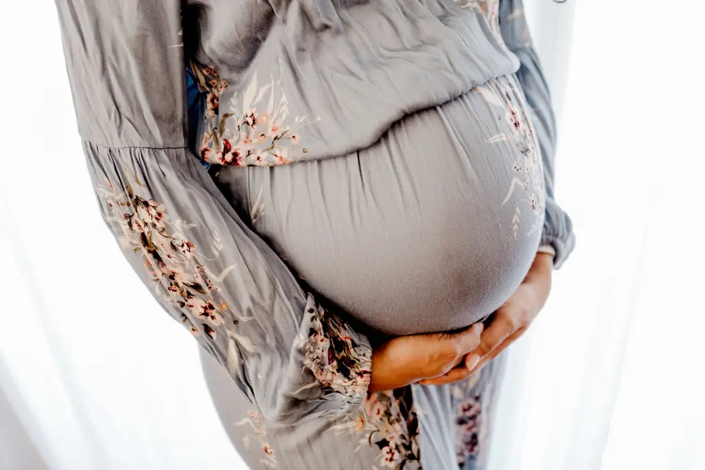 Gravid kvinna i blommig klänning håller händerna under magen, under graviditeten när gravidförsäkringen ska tecknas