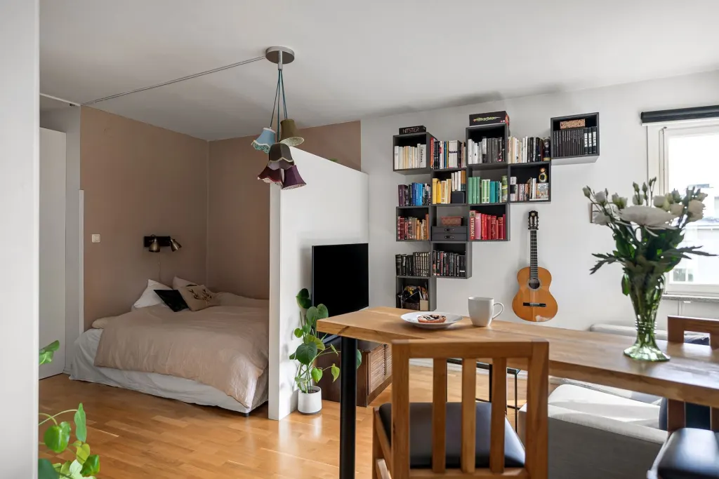 Liten etta med säng, bokhylla, gitarr och matbord av trä, ett typiskt studentboende