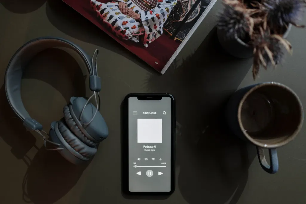 Mobiltelefon som spelar en podd mellan hörlurar och en kaffekopp på ett mörkt bord, musik och poddar kräver lite surf jämfört med video