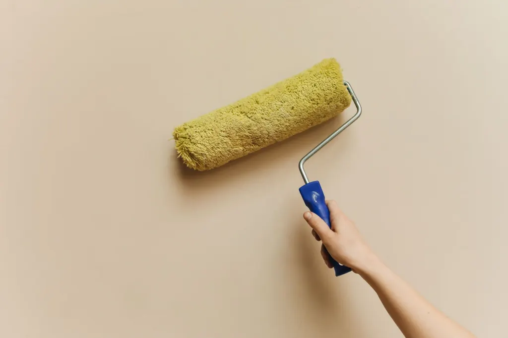 En hand som målar en beige vägg med en målarroller, en bild för att låna till renovering av bostaden