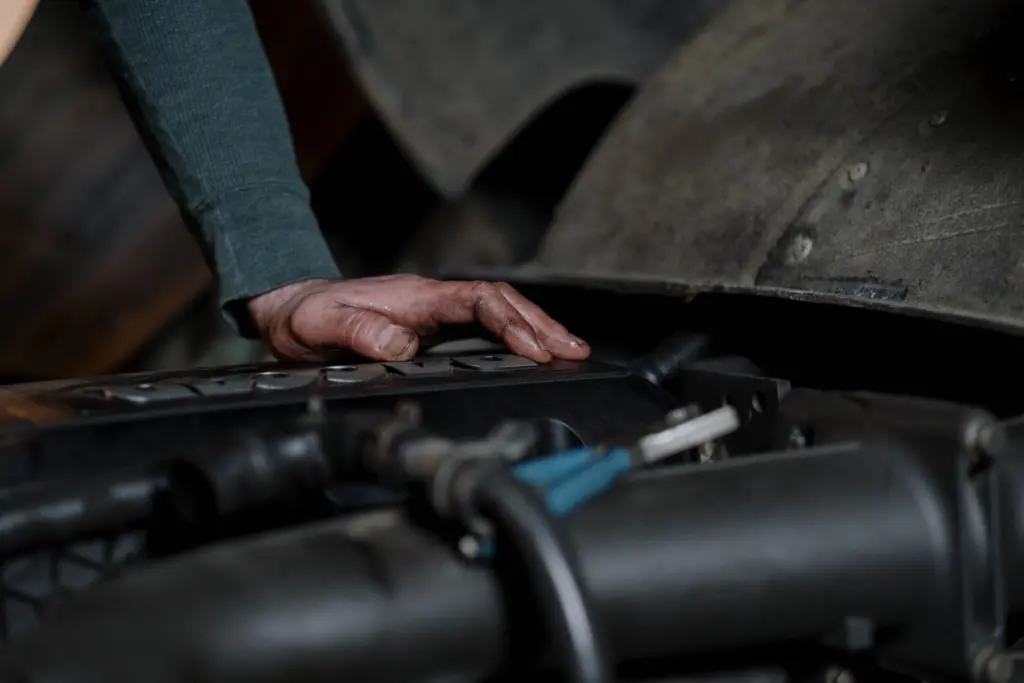 Mekanikers hand med oljiga fingrar vilar på en motor under en öppen motorhuv i en verkstad
