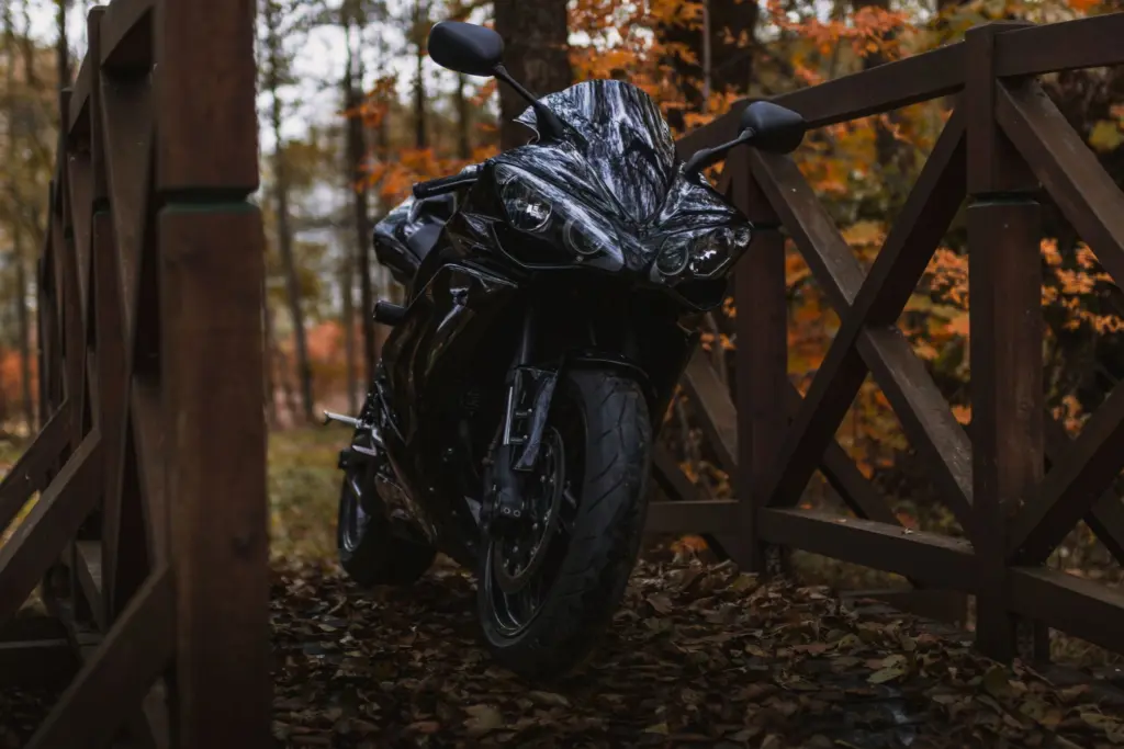 Svart motorcykel parkerad på en träbro i en skog med höstlöv, när säsongen går mot sitt slut och det är dags att välja mellan avställning och årsförsäkring