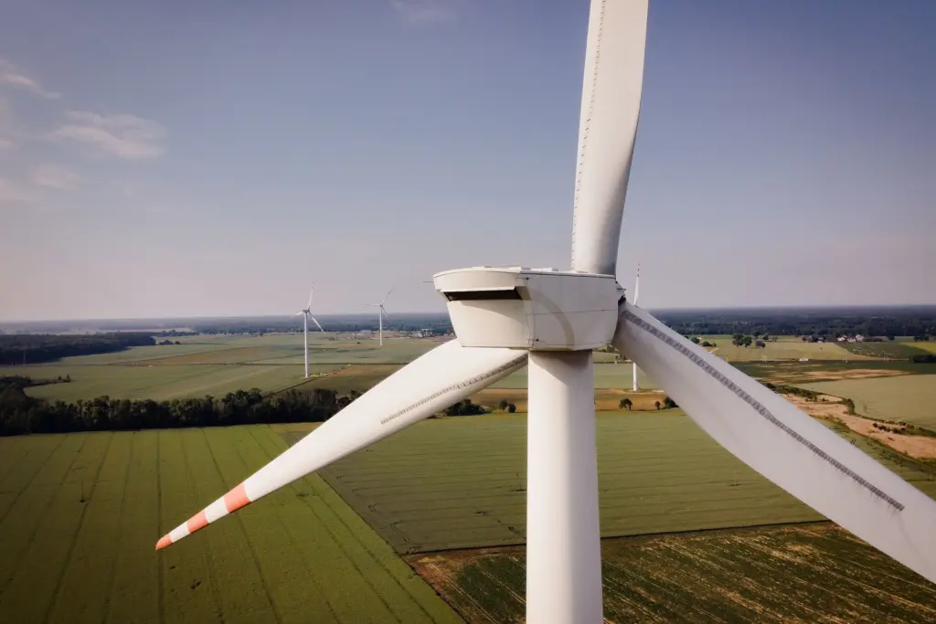 Vindkraftverk i förgrunden med fler vindkraftverk över gröna åkrar, sett från ovan