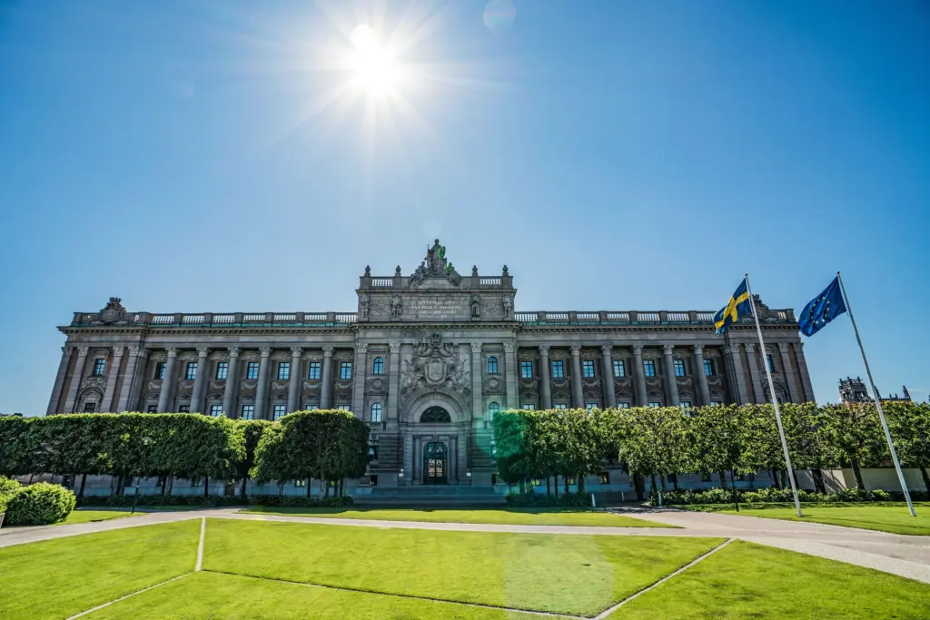 Riksdagshuset i Stockholm med svensk flagga och EU-flagga en solig dag, riksdagen beslutade om den nya konsumentkreditlagen