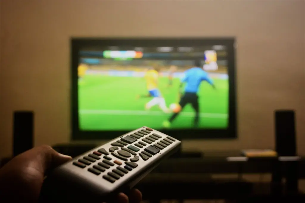 En hand håller en fjärrkontroll framför en tv som visar en fotbollsmatch