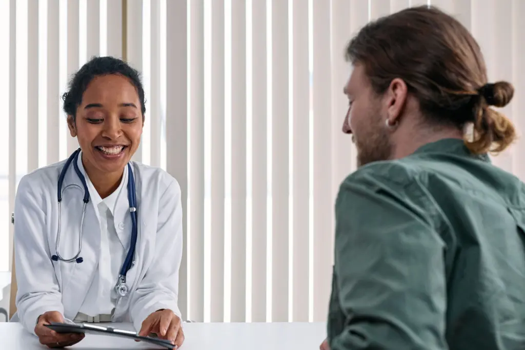 Läkare i vit rock går igenom papper med en patient vid ett skrivbord på en ljus mottagning