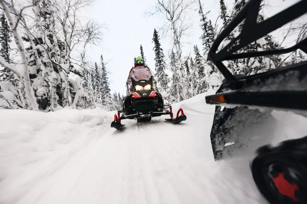 Snöskoter med strålkastarna tända på en led genom snötäckt björk- och granskog