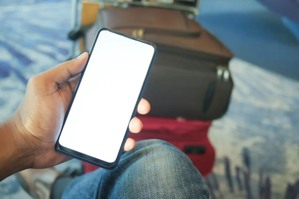 Hand som håller en mobiltelefon framför resväskor på en flygplats, inför att surfa utomlands
