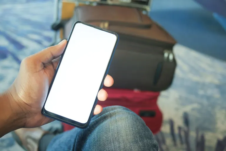 Hand som håller en mobiltelefon framför resväskor på en flygplats, inför att surfa utomlands