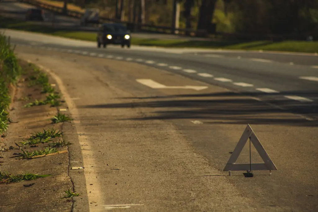 Varningstriangel utställd på vägen vid ett motorstopp medan en bil närmar sig i kvällsljuset