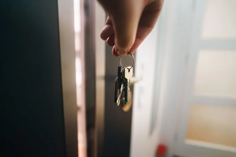 Hand som håller upp en nyckelknippa framför en öppen ytterdörr, hemförsäkringen skyddar det du har innanför dörren