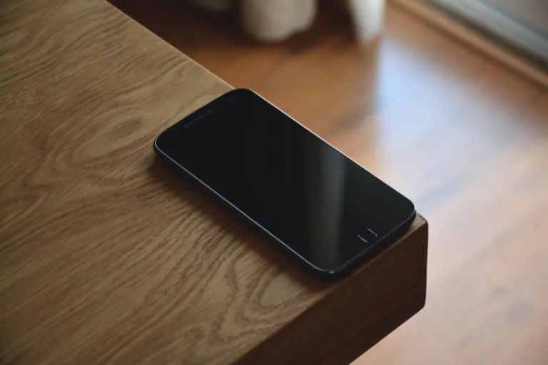 Svart smartphone med släckt skärm på kanten av ett träbord, det billigaste mobilabonnemanget räknas på snittpriset för hela första året