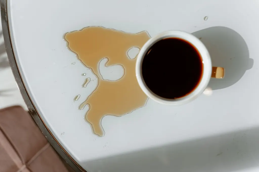 Utspillt kaffe bredvid en kopp på ett vitt bord, en typisk vardagsolycka som drulleförsäkring kan ersätta