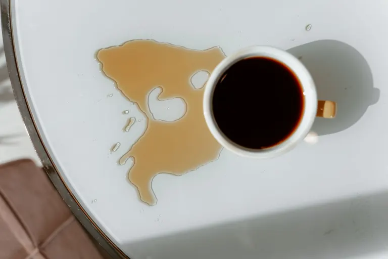 Utspillt kaffe bredvid en kopp på ett vitt bord, en typisk vardagsolycka som drulleförsäkring kan ersätta