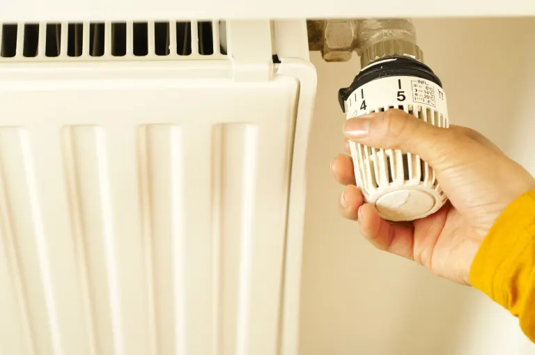 Hand som vrider på termostaten till ett vitt element, uppvärmningen påverkar vad elen kostar per månad