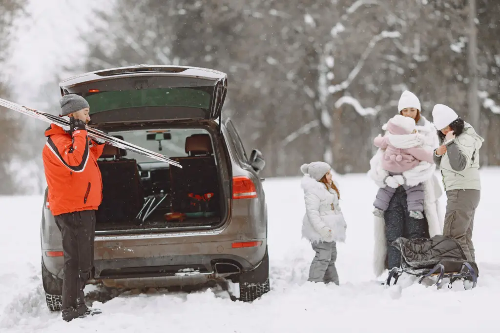 Familj med barn packar skidor och pulka i bilen en snöig vinterdag, där hemmet, bilen och barnen alla behöver rätt försäkring