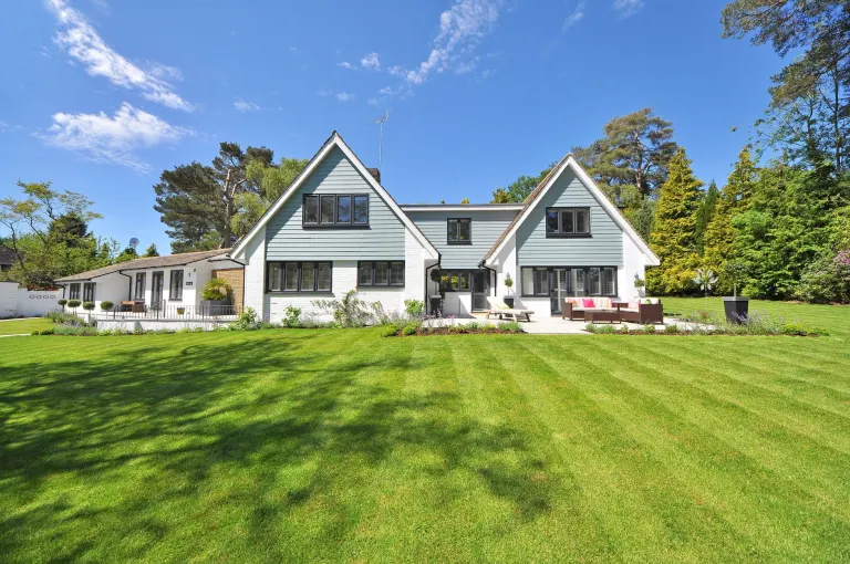 Vit villa i trä med stor gräsmatta och trädgård en sommardag