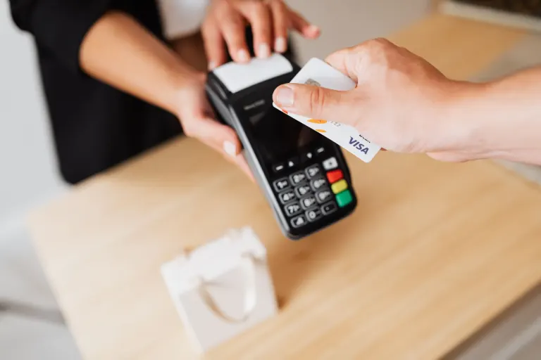Hand blippar ett kreditkort mot en kortterminal på en butiksdisk i trä