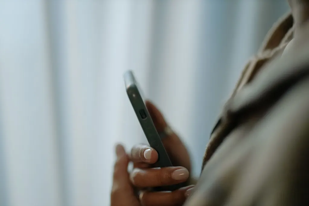 Person håller sin mobil i handen vid ett ljust fönster, en bild för att jämföra mobilabonnemang