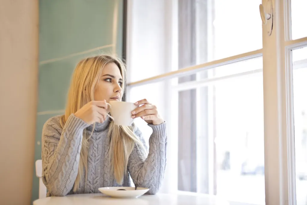 Kvinna med kaffekopp vid fönstret tar en lugn paus innan hon bestämmer sig om ett snabblån