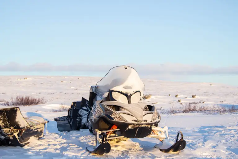 Snöskoter med släde parkerad på ett snötäckt fjäll i vinterljus, en bild för snöskoterförsäkring