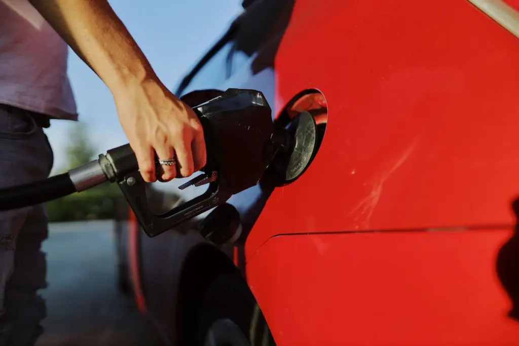 Person tankar en röd bil vid bensinpumpen