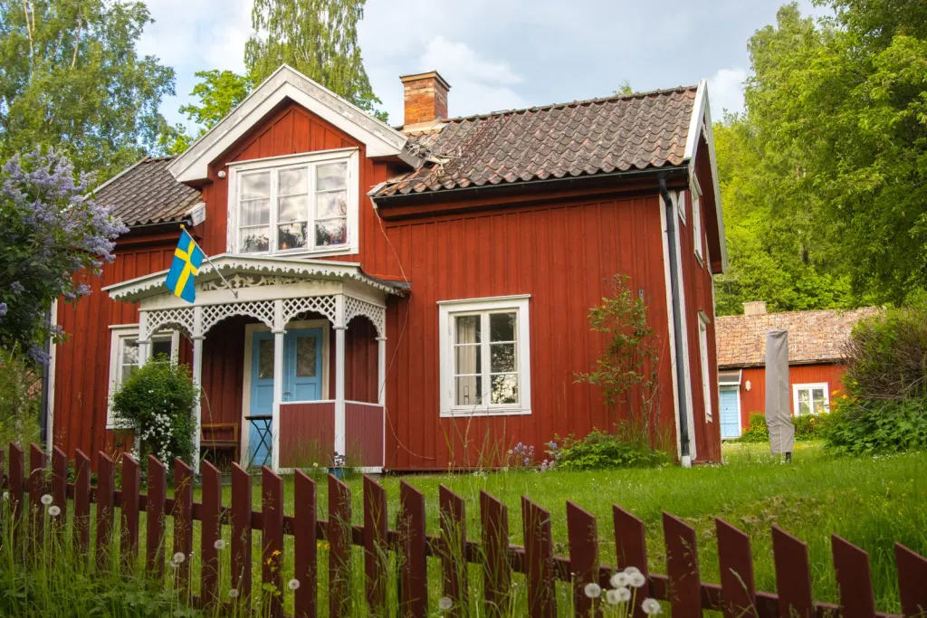 Rödmålad trävilla med vita knutar, staket och svensk flagga i trädgården, skyddad av villaförsäkring